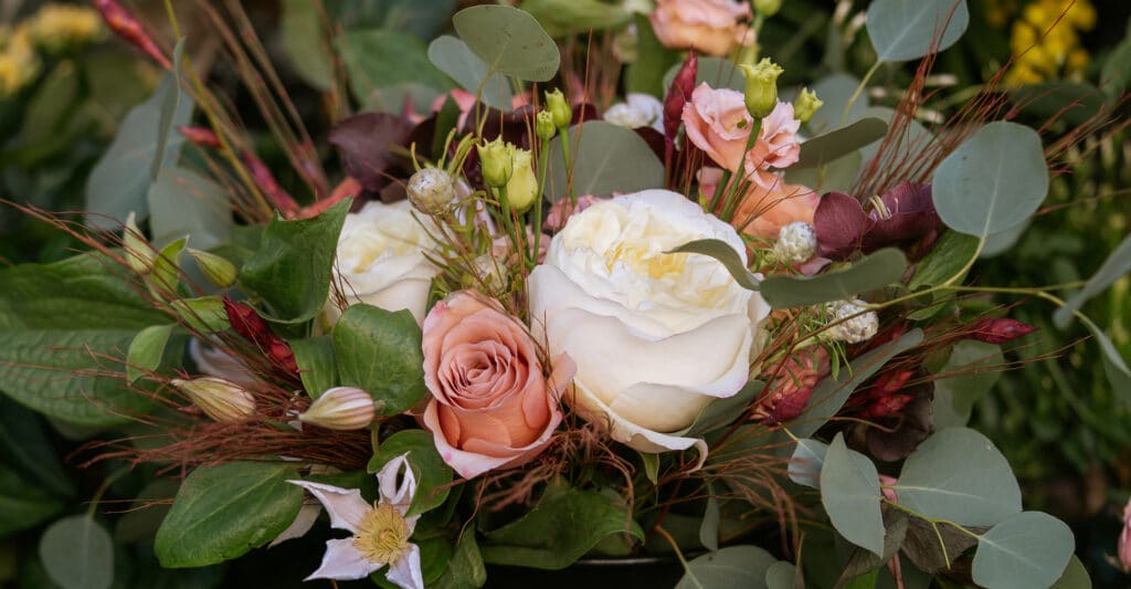 Grand bouquet élégant de roses blanches, roses pêche, lisianthus, clematite, eucalyptus et feuillage vert foncé. Ambiance naturelle et douce.