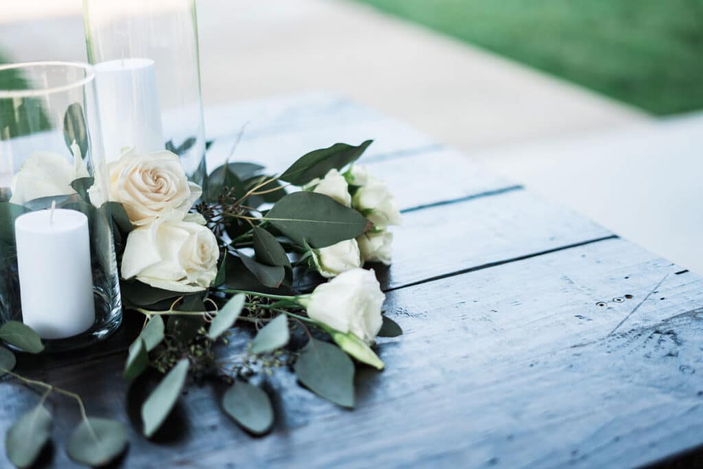 Arrangement élégant de roses blanches, eucalyptus et bougies cylindriques dans des vases en verre, posé sur une table en bois rustique.